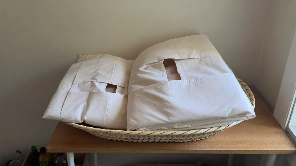Folded pale linens in a woven basket on a wooden counter.